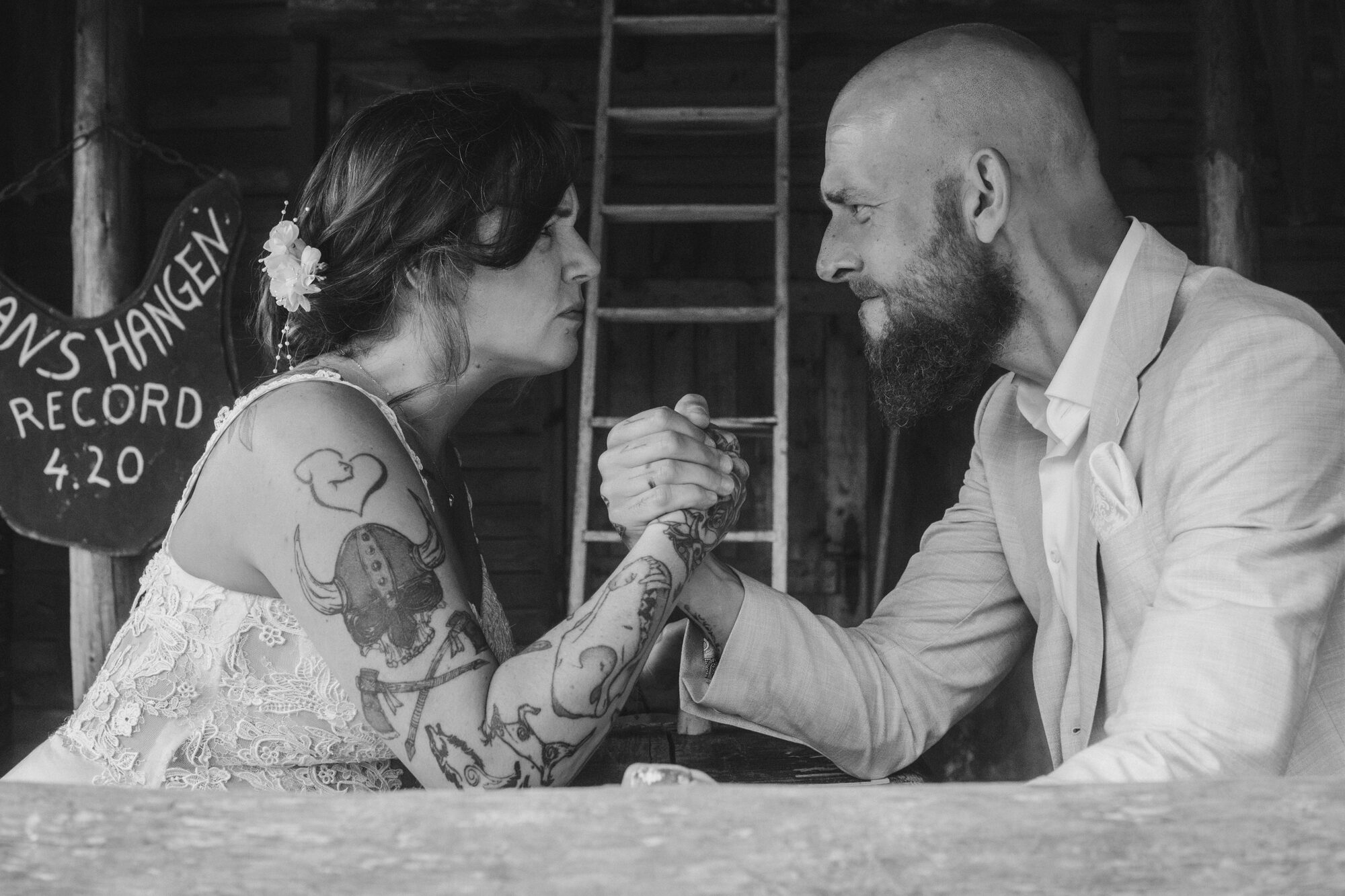 Newlyweds arm wrestling across a table in black and white